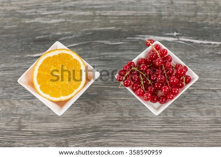 A closeup view from a sliced orange fruit and a berry bush in a bowl on a wooden table.