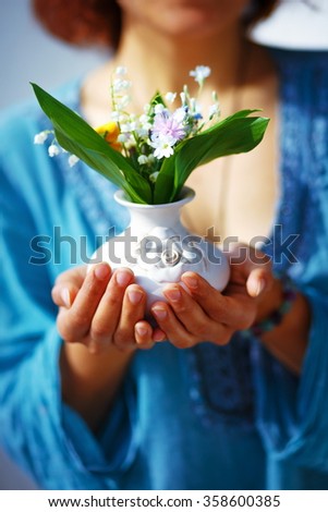 Woman holding bouquet of flower in vase. Blue clothing background