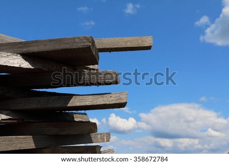 Ends of the rough pine boards in the outdoor stack against a blue sky