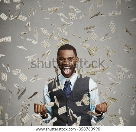 Portrait happy man exults pumping fists ecstatic celebrates success screaming under money rain falling down dollar bills banknotes isolated gray background with copy space. Financial freedom concept  