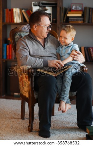 Grandfather sitting in armchair and reading book to his grandson