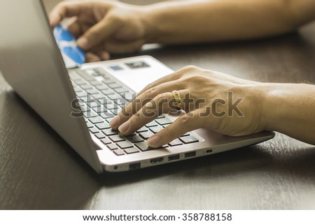 Close Up Of A Man Shopping Online Using Laptop With Credit Card,male hands holding credit card typing numbers on computer keyboard  at the wooden table,selective focus and vintage color.