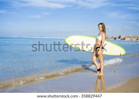 Beautiful young woman holding her surfboard and ready to surf