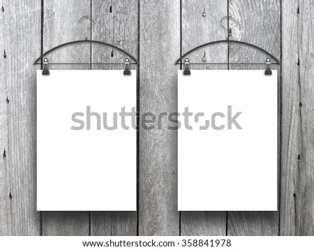 Close-up of two hanged paper sheets with metallic clothes hanger on grey vertical wooden boards background