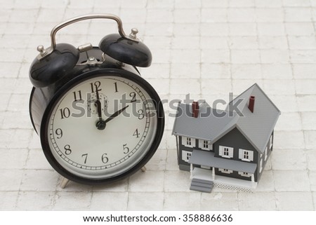 Time to buy a house, A gray house and black alarm clock on stone background