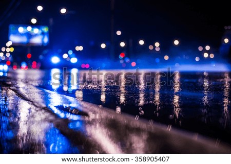 Rainy night in the big city, the light from the headlamps of approaching car on the highway. View from the level of the dividing line, in blue tones