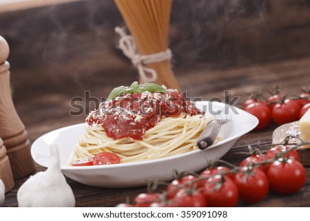 Warm, delicious spaghetti with sauce and basil on wooden table.