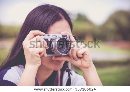 Female photographer with sunglasses holding professional digital camera vintage style. Asian woman taking picture on blurred nature background. Outdoor.