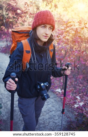 The girl with the camera and the backpack goes on the trail in a beautiful forest.
