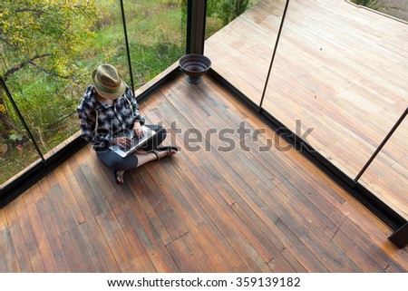 Casual dressed person sitting on Wood Floor of Rural Bungalow and working on Laptop