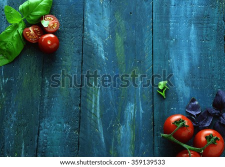 Fresh vine tomatoes and basil leaves as cooking ingredients with a halved cherry tomato on dark background with copyspace