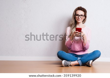 Happy beautiful woman sitting on the floor and using smartphone Royalty-Free Stock Photo #359139920
