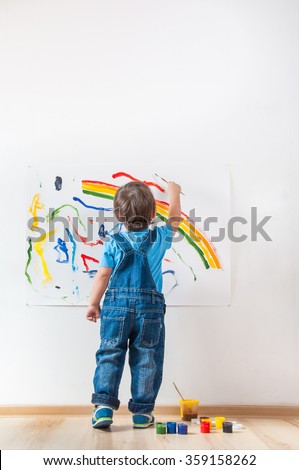 child draws colored paint spots on paper