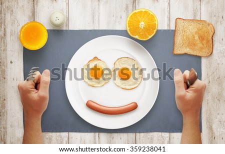 Breakfast with a smile of plate. Eggs, hot dog, orange, juice, toast on table with a top view.