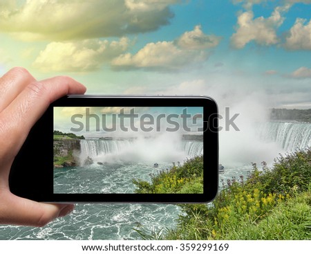 Female hand with smartphone taking a picture of Niagara Falls. Tourism concept