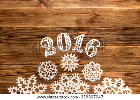 Happy new year 2016 written figures carved from a white sheet on the wooden background with Christmas snowflakes, with space for text