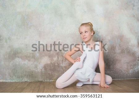 Little ballet dancer doing stretching before class in a white bathing suit, dance, sports, healthy lifestyle, ballet
