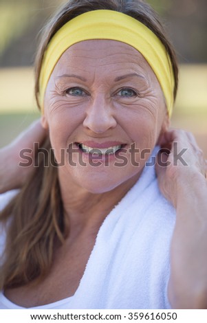 Portrait active fit sporty attractive mature woman, happy confident smile, towel, headband, exercising outdoors, blurred background.