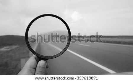 hand holding magnifying glass in black and white on a free highway. nature composition                                
