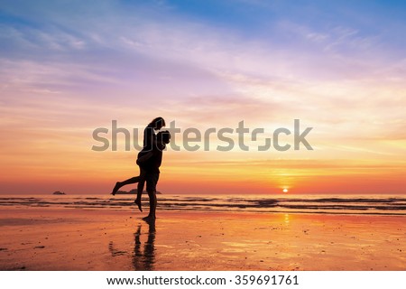 Couple kissing on the beach with a beautiful sunset in background, man lifting the woman Royalty-Free Stock Photo #359691761