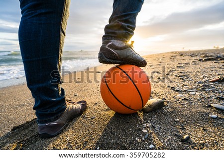 Woman standing on the beach at sunset, basketball