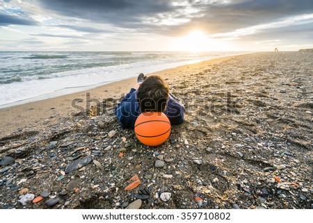 Man lying on the beach in the evening with a basketball  
