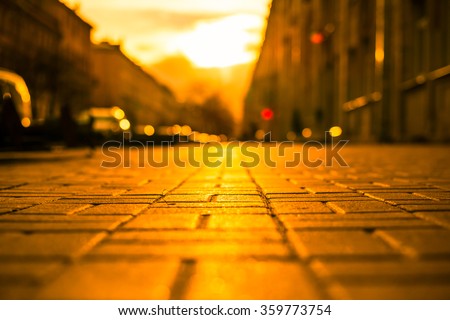 Streets in the light of the autumn sun, pedestrians walk on the sidewalk. The view from the sidewalk level, image in the orange-yellow toning