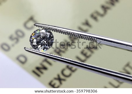 cut diamond held by tweezers above certificate Royalty-Free Stock Photo #359798306