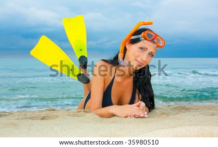 Beach lying woman with diving equipment and diving fins relaxing smiling and looking cheerful with ocean and blue sky in background