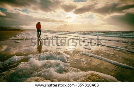 A woman walking alone on the beach. This image has added grain and styling. Royalty-Free Stock Photo #359810483