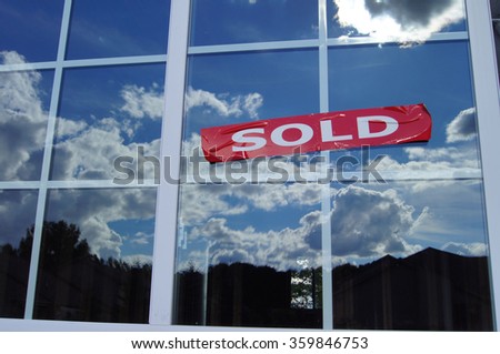 Sold sign on window of new construction home with muntin bars and clouds in background on blue sky