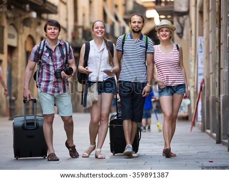 Two cheerful young traveler couples with travel bags walking through the city. Selective focus
