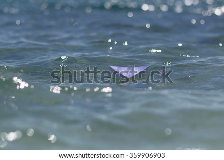 Photo closeup of one white paper origami boat riding on blue salt sea waves ocean water surface with ripples on blurred bokeh seascape background, horizontal picture 