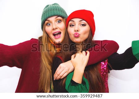 Two young teenage hipster girl friends together.Close up fashion portrait of two sisters hugs and having fun winter time,wearing bright hats,scarfs and sweater,best friends couple at white background 