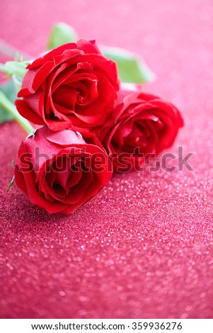 Three red roses over pink glittering background 
