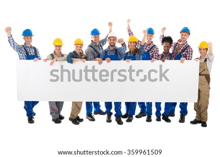 Full length portrait of happy carpenters with arms raised holding blank billboard against white background