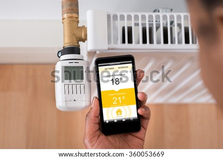 Close-up Of A Person's Hand Adjusting Temperature On Thermostat Using Cellphone