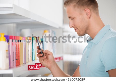 Male customer photographing cosmetic product arranged on shelf in supermarket