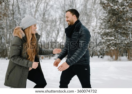 Cute young hipster couple having fun in winter park on a bright day hugging each other and smiling