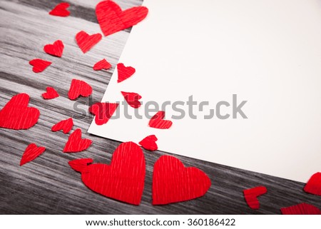 white sheet of paper and a lot of little red hearts on a wooden background, the concept of Valentine's Day