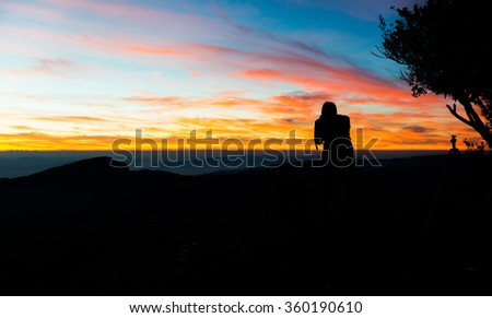 silhouette of photographer taking picture of landscape during sunset on mountain