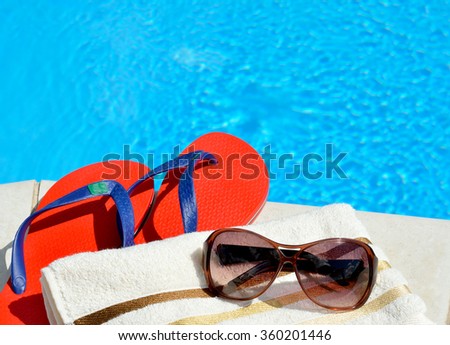 Sunglasses, beach towel and flip-flops by the swimming pool.
