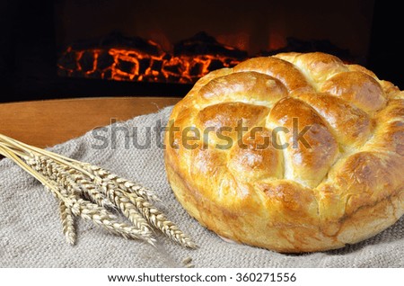 Fresh home made bread set on jute cloth with a bunch of dry wheat ears and fireplace in background