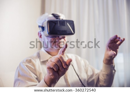 Close-up shot of the silver-haired man  dressed in a glasses of virtual reality in a bright room at home
