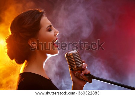 Elegant woman singing in colourful smoke, close up Royalty-Free Stock Photo #360322883