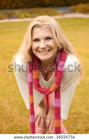 Picture of a funny cute girl smiling on the autumn lawn in a magenta scarf