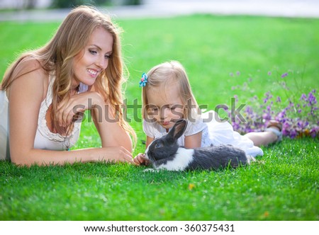 Young woman and her daughter playing with a pet rabbit in a park