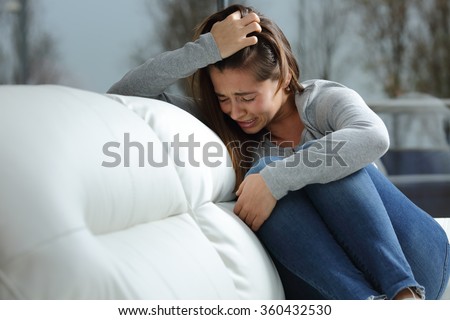 Sad girl crying desperately alone sitting on a couch at home in a dark winter day Royalty-Free Stock Photo #360432530