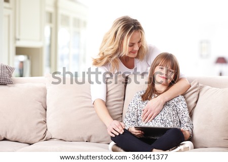 Portrait of a beautiful happy mother and her cute daughter sitting at living room together and looking digital tablet together.