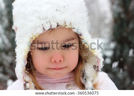 Happy toddler girl in warm coat and knitted hat dreaming in the winter forest, outdoor portrait, winter family concept